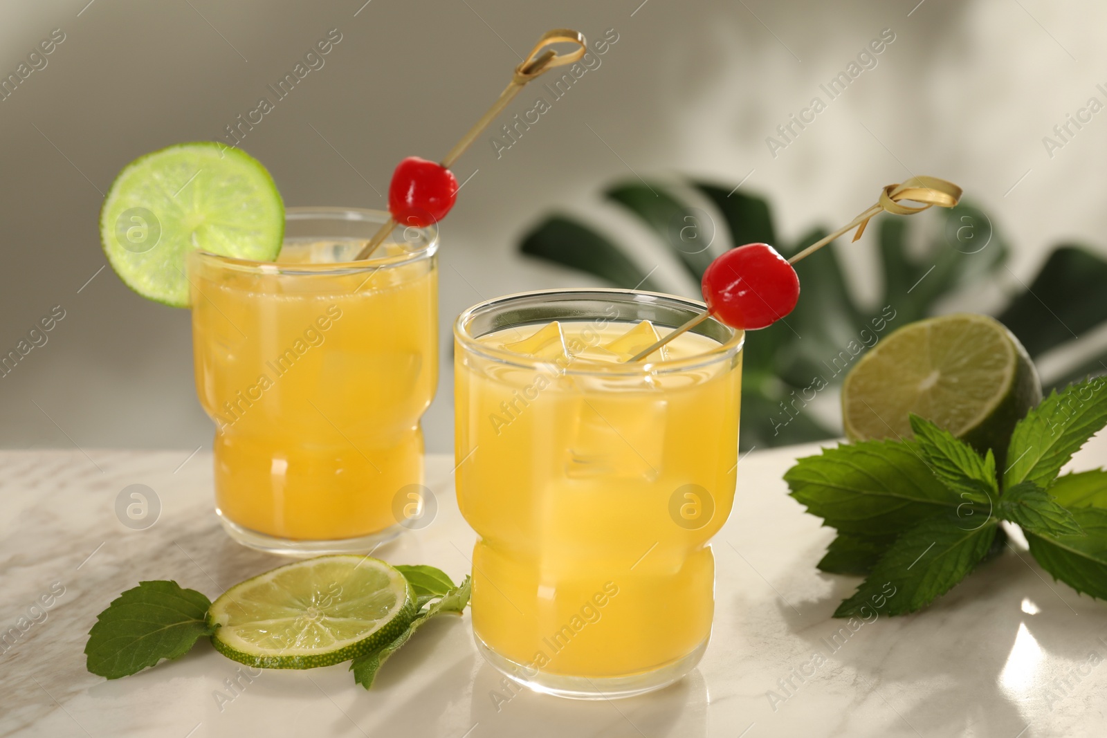 Photo of Glasses of tasty pineapple cocktail with cherry, lime and mint on white table