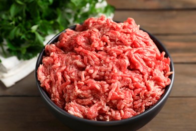 Photo of Raw ground meat in bowl and parsley on wooden table, closeup