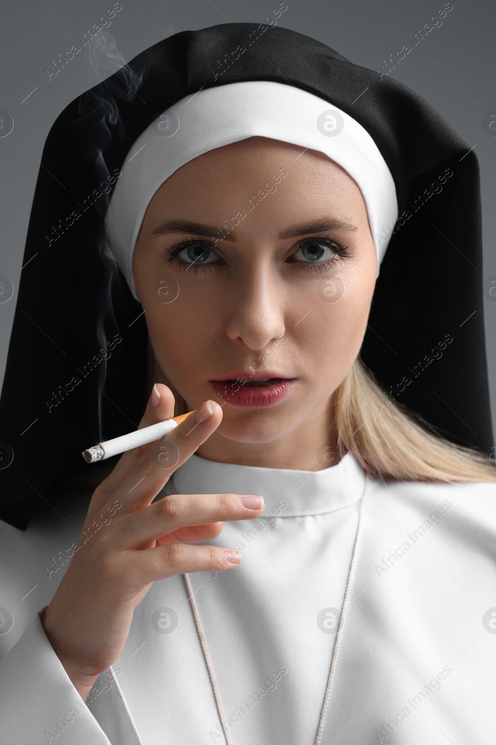 Photo of Woman in nun habit smoking cigarette on grey background, closeup