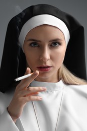 Woman in nun habit smoking cigarette on grey background, closeup