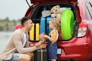 Photo of Father and daughter near car trunk with suitcases outdoors