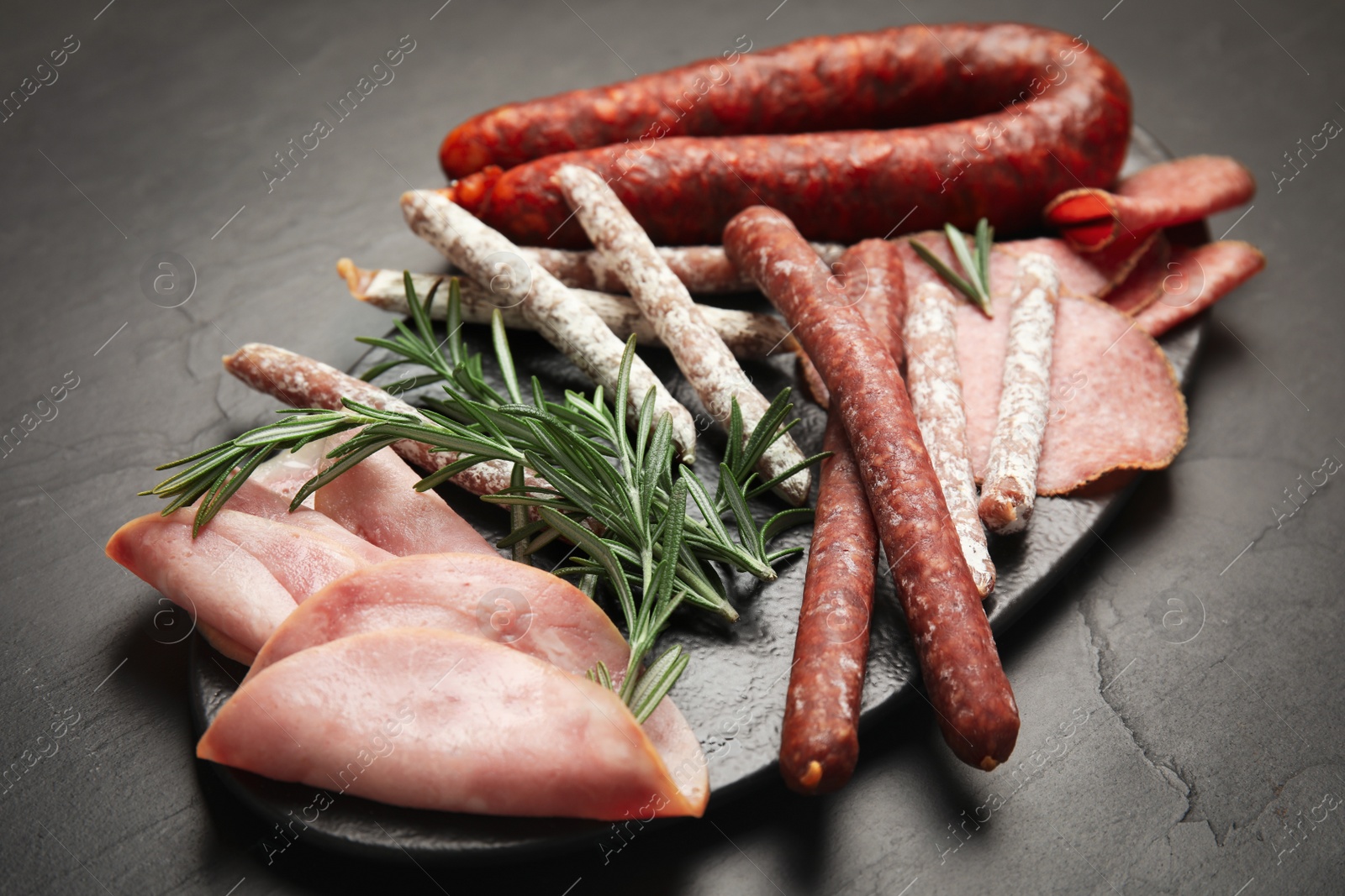 Photo of Different tasty sausages and rosemary on black table