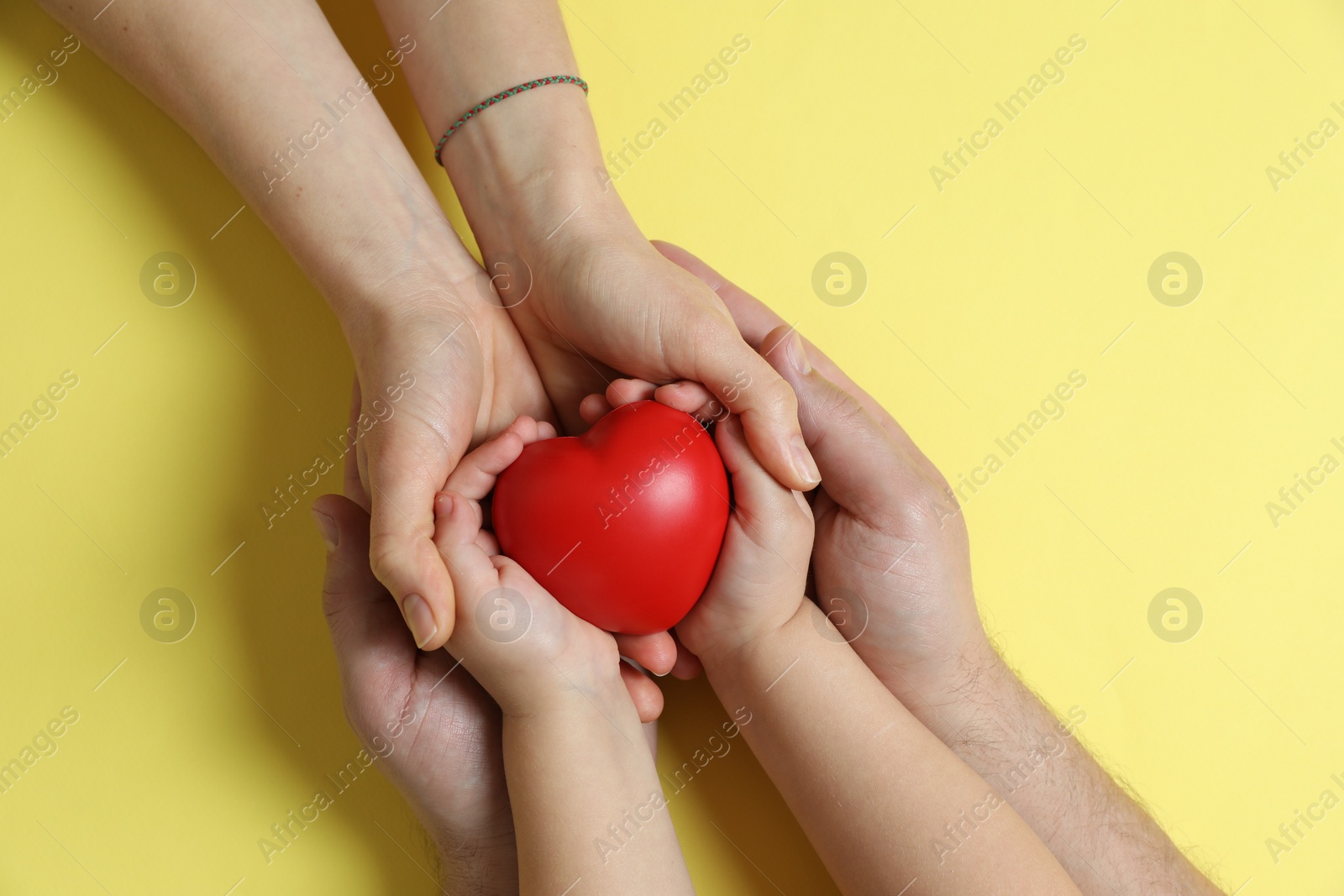 Photo of Parents and child holding red decorative heart on pale yellow background, top view