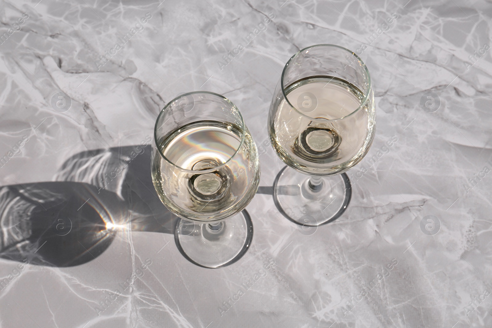 Photo of Glasses of white wine served on grey marble table, above view