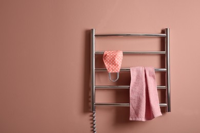 Modern heated towel rail with cloth face mask and towel on light pink wall. Space for text