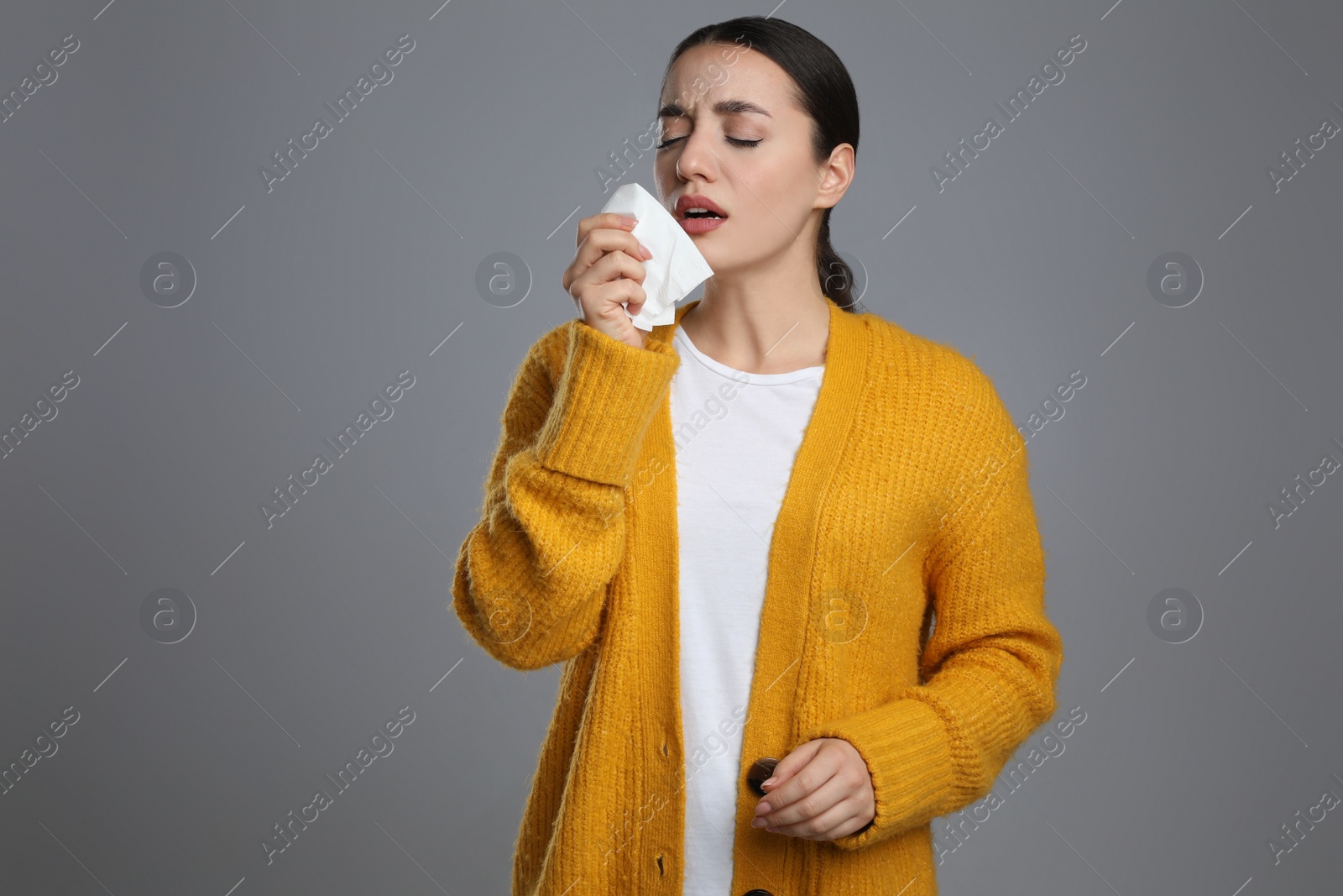 Photo of Sick young woman sneezing in tissue on grey background. Cold symptoms