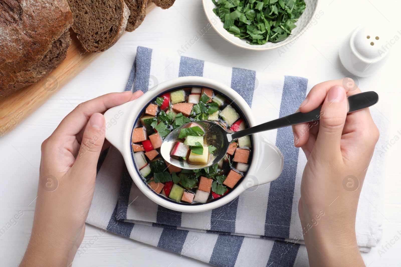 Photo of Woman eating delicious cold okroshka with kvass at white wooden table, top view. Traditional Russian summer soup