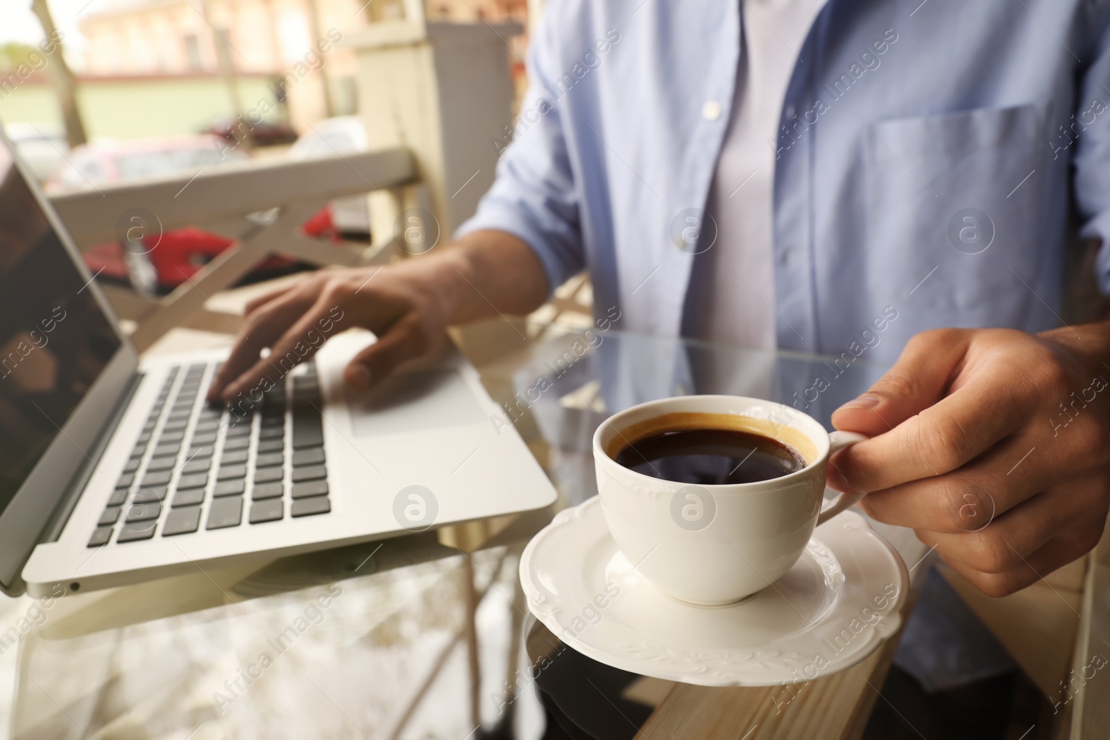 Photo of Man with cup of coffee working on laptop at outdoor cafe in morning, closeup