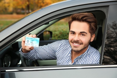 Photo of Young man holding driving license in car