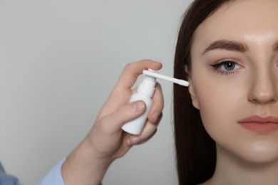 Man spraying medication into woman`s ear on light grey background, closeup. Space for text