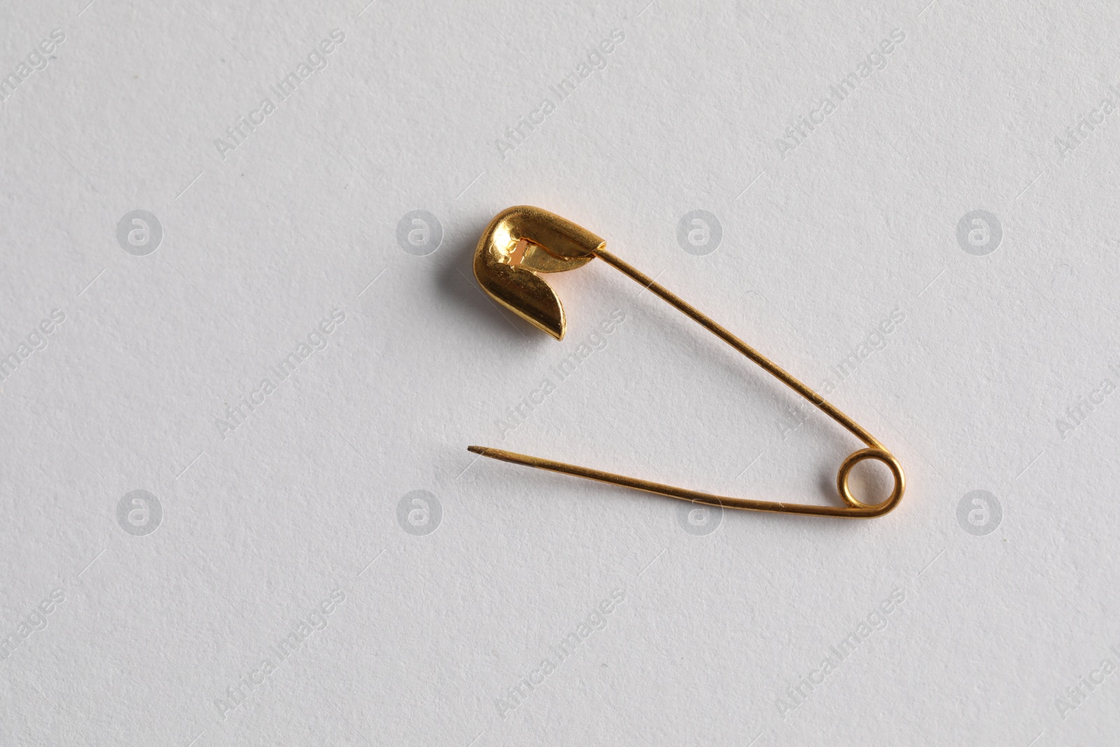 Photo of Golden safety pin on white background, top view