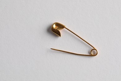 Photo of Golden safety pin on white background, top view