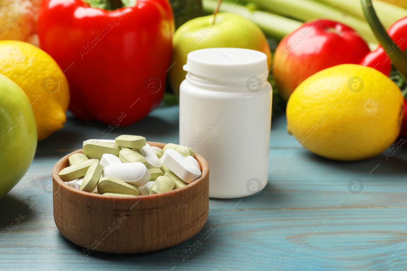 Photo of Dietary supplements. Blank white bottle and bowl with different pills near food products on light blue wooden table, closeup