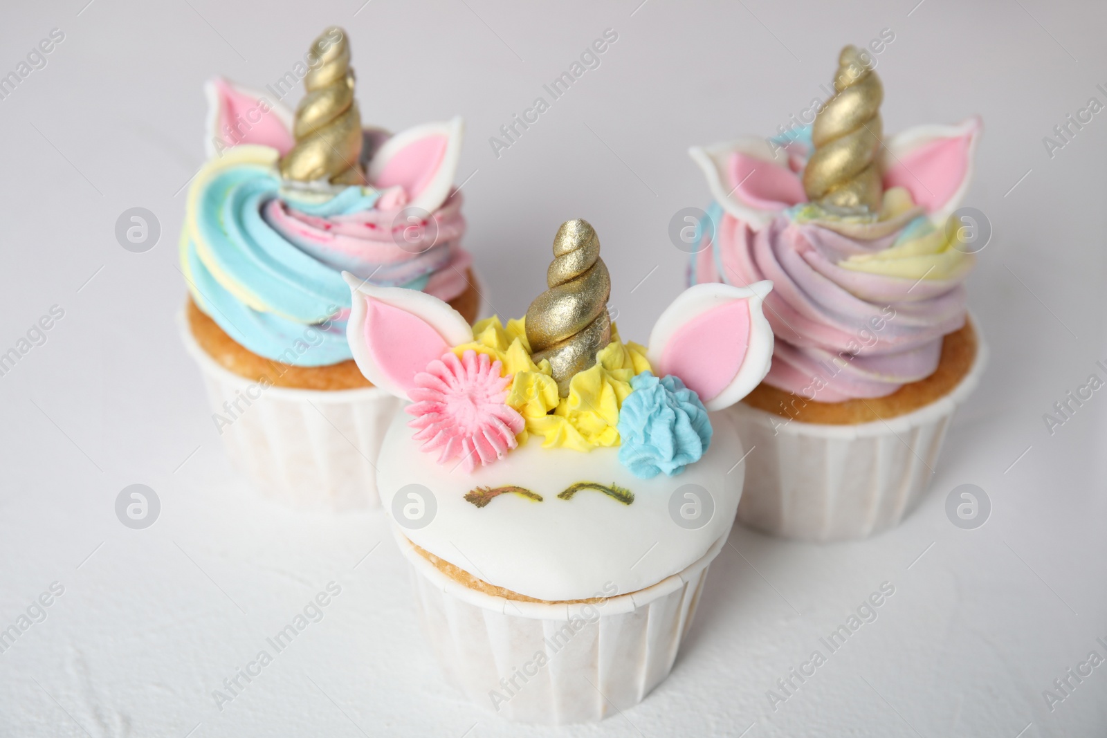 Photo of Three cute sweet unicorn cupcakes on white table