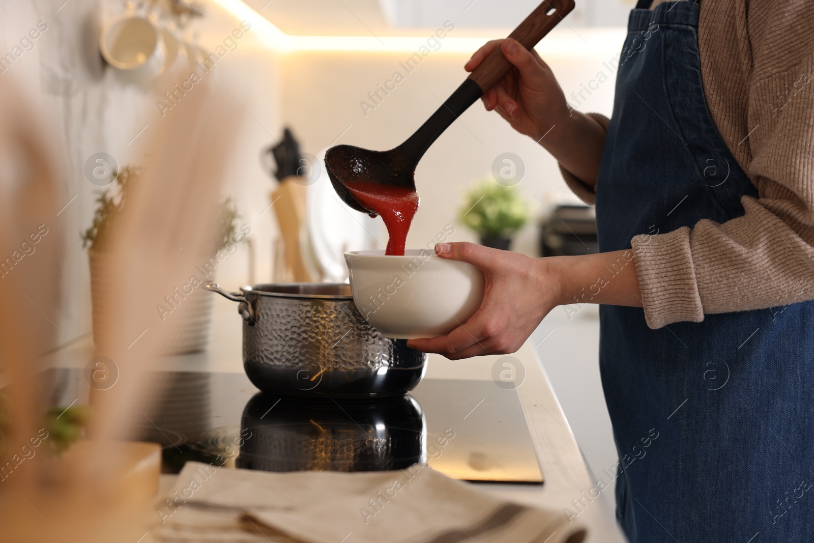 Photo of Woman pouring tasty soup into bowl at countertop in kitchen, closeup