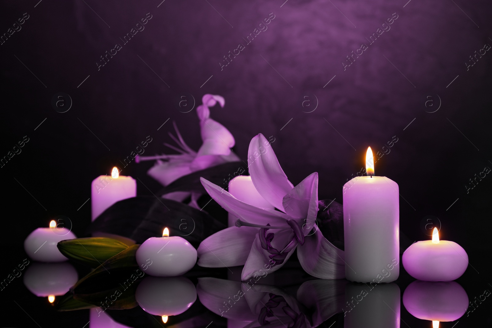 Image of Violet lilies and burning candles on black mirror surface in darkness. Funeral attributes