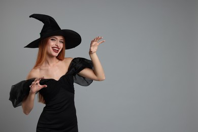 Photo of Happy young woman in scary witch costume on light grey background, space for text. Halloween celebration