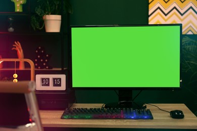 Modern computer and RGB keyboard on wooden table indoors. Mockup green screen