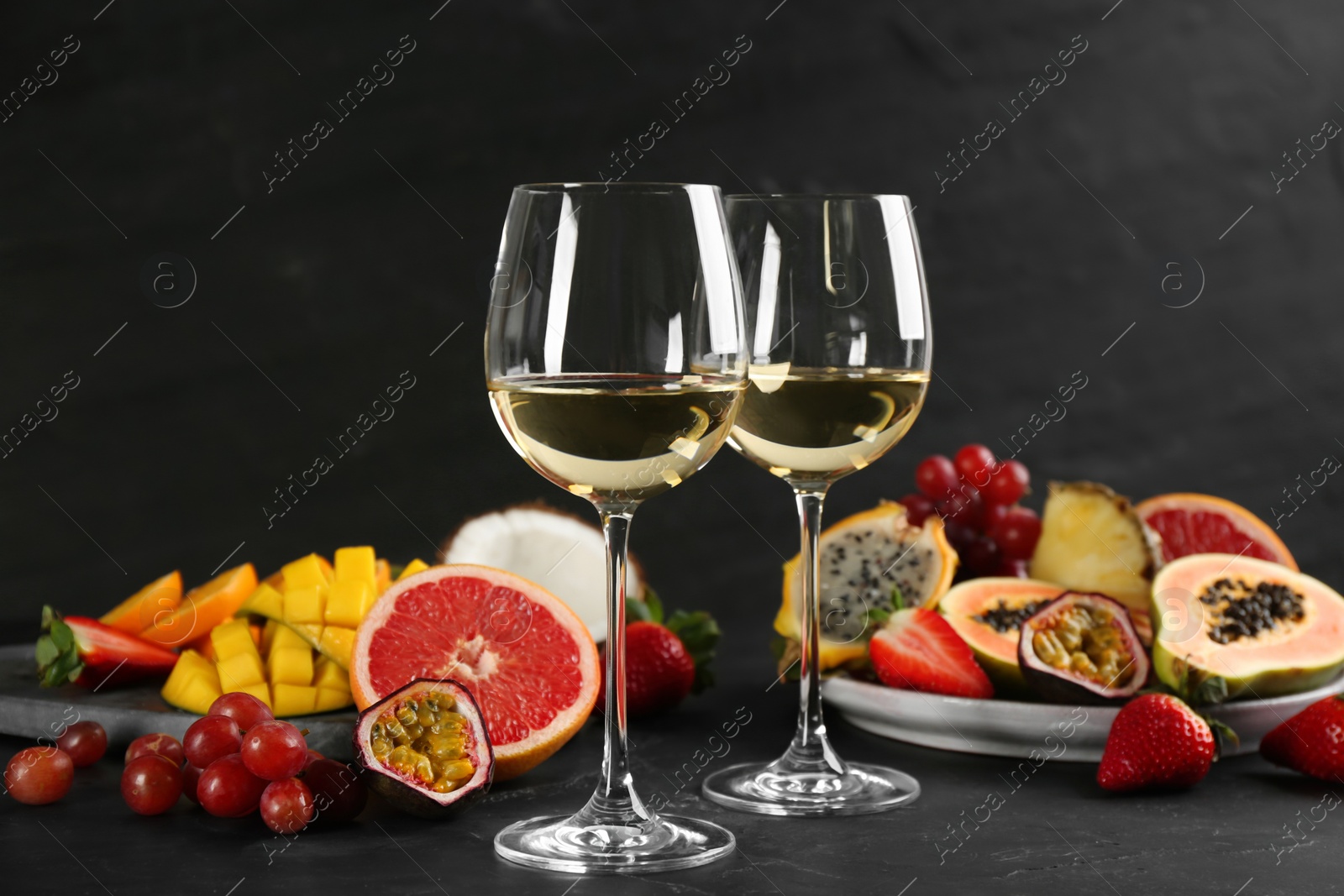 Photo of Delicious exotic fruits and glasses of wine on black table