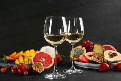 Delicious exotic fruits and glasses of wine on black table