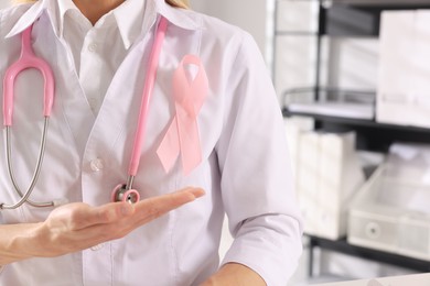 Photo of Doctor with stethoscope and pink ribbon indoors, closeup. Breast cancer awareness