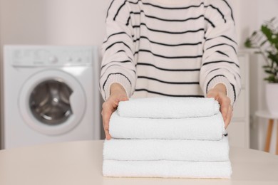 Photo of Woman with stack of folded towels at white table in laundry room, closeup. Space for text