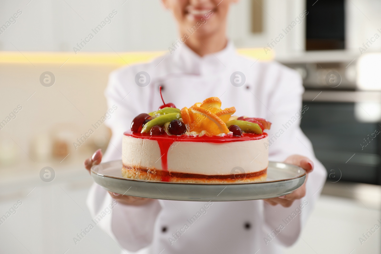 Photo of Happy professional confectioner holding delicious cake in kitchen, closeup