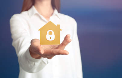 Image of Home security concept. Woman holding house on color background, closeup