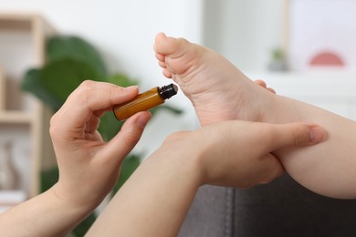 Mother applying essential oil from roller bottle onto her baby`s heel indoors, closeup