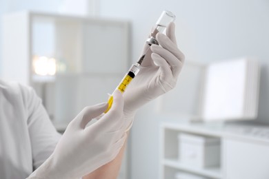 Doctor filling syringe with medication from vial in hospital, closeup