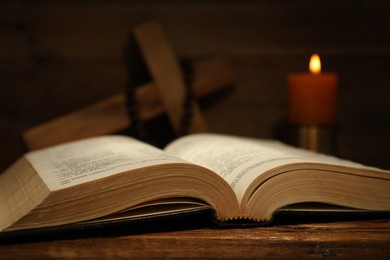 Photo of Bible, cross, rosary beads and church candle on wooden table, closeup