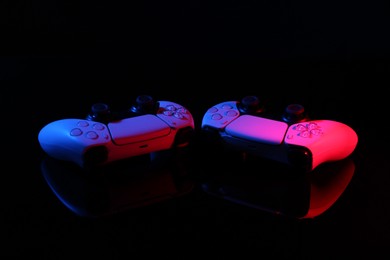 Wireless game controllers on black mirror surface in neon lights