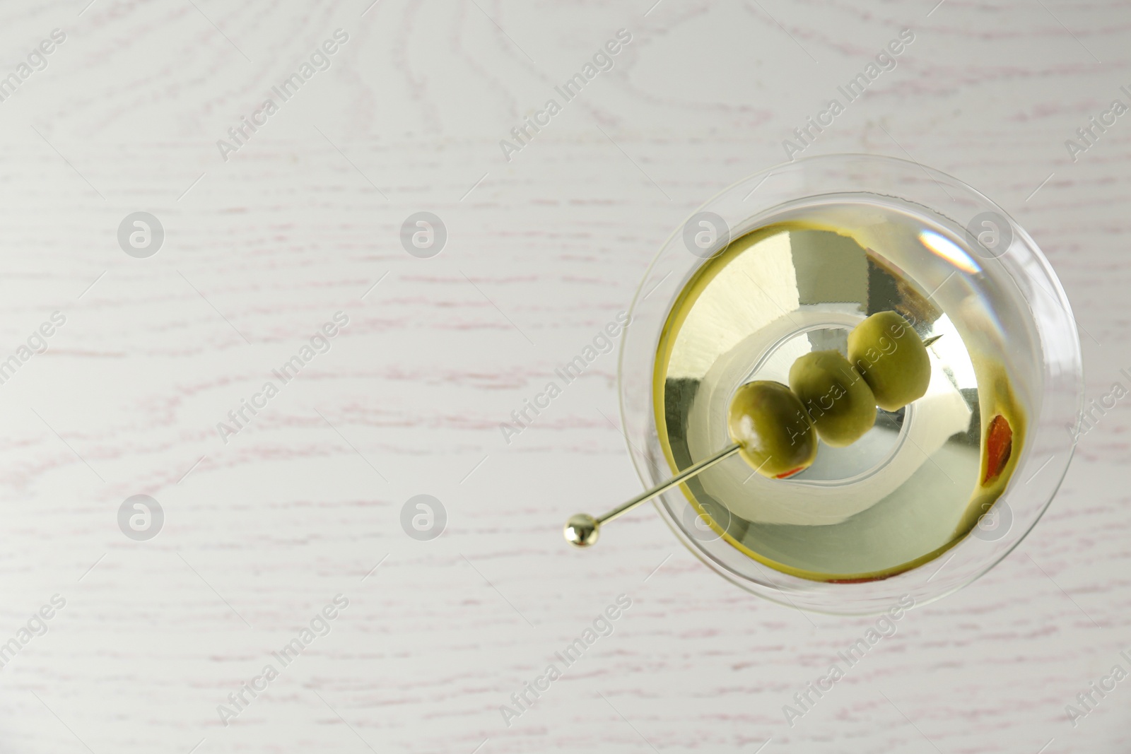 Photo of Glass of Classic Dry Martini with olives on wooden table, top view. Space for text