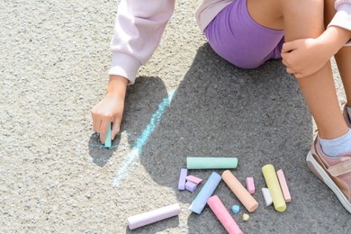 Photo of Little child drawing flower with chalk on asphalt, closeup