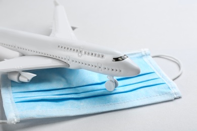Photo of Toy airplane and protective mask on light background, closeup. Travelling during coronavirus pandemic