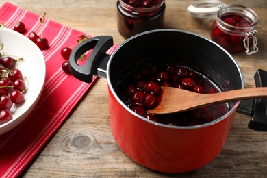 Photo of Pot with cherries in sugar syrup on wooden table. Making delicious jam
