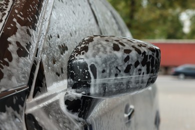 Automobile side-view mirror with cleaning foam at car wash, closeup