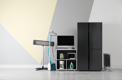 Modern refrigerator and other household appliances near color wall indoors
