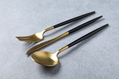 Photo of Stylish golden cutlery. Fork, spoon and knife on grey table