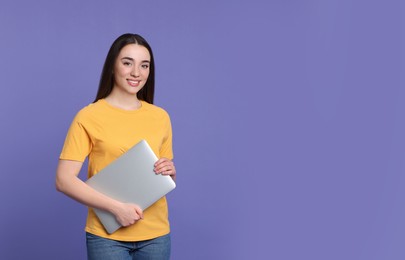 Smiling young woman with laptop on lilac background, space for text