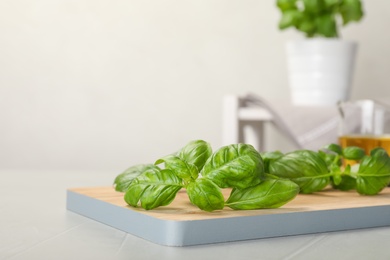 Wooden board with fresh green basil leaves on table. Space for text