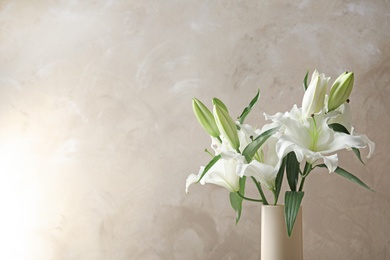 Photo of Vase with beautiful lilies on light brown background, space for text