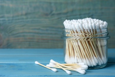 Many cotton buds on light blue wooden table, space for text