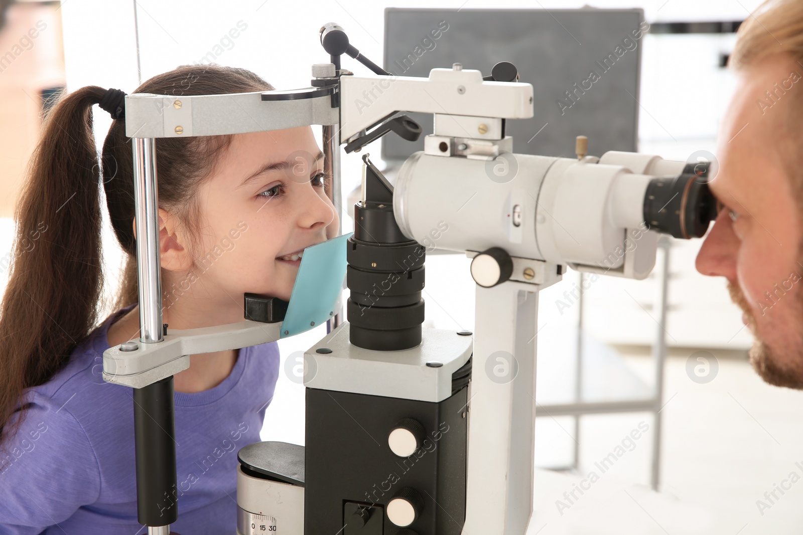 Photo of Children's doctor examining little girl with ophthalmic equipment in clinic