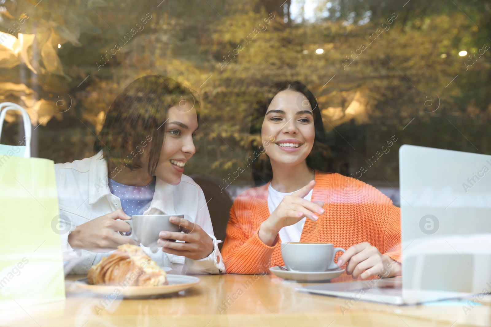 Photo of Special Promotion. Happy young women using laptop at table in cafe, view from outdoors