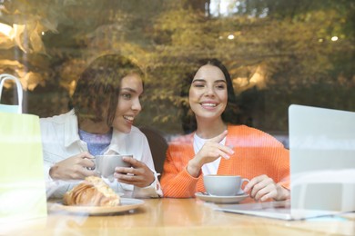 Special Promotion. Happy young women using laptop at table in cafe, view from outdoors