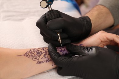 Photo of Professional artist making tattoo on hand at table, closeup