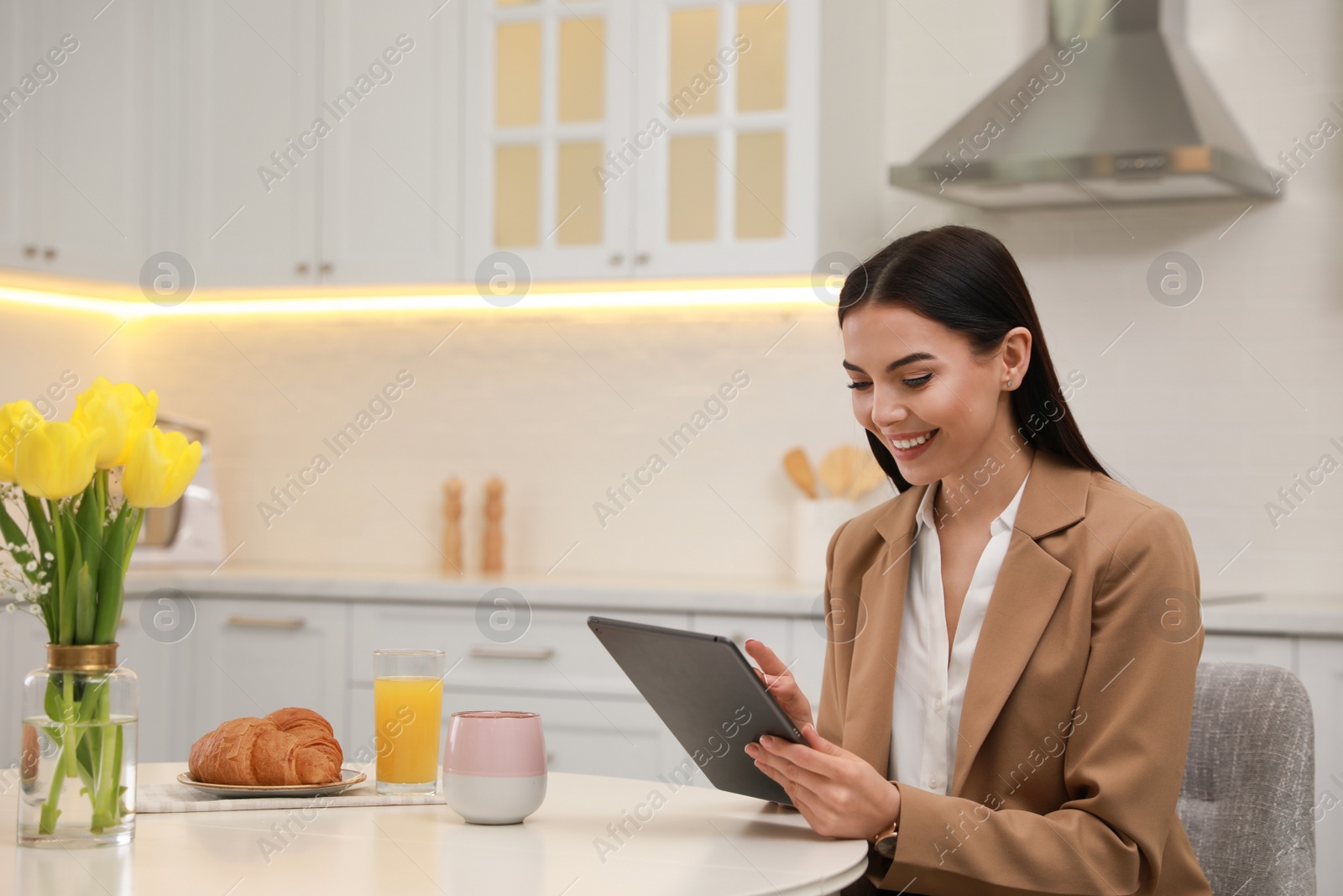 Photo of Young woman with tablet having breakfast in kitchen. Morning routine