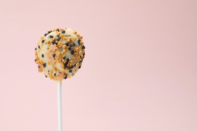 Delicious confectionery. Sweet cake pop decorated with sprinkles on pale pink background, closeup. Space for text