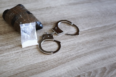 Drugs with handcuffs on wooden background, space for text. Criminal law